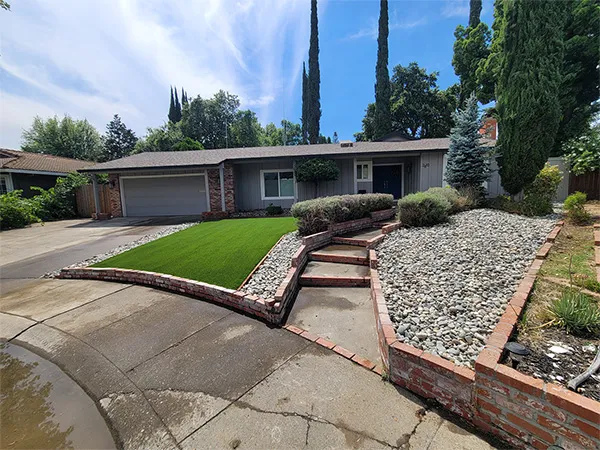 Front yard turf conversion framed by a low brick planter wall