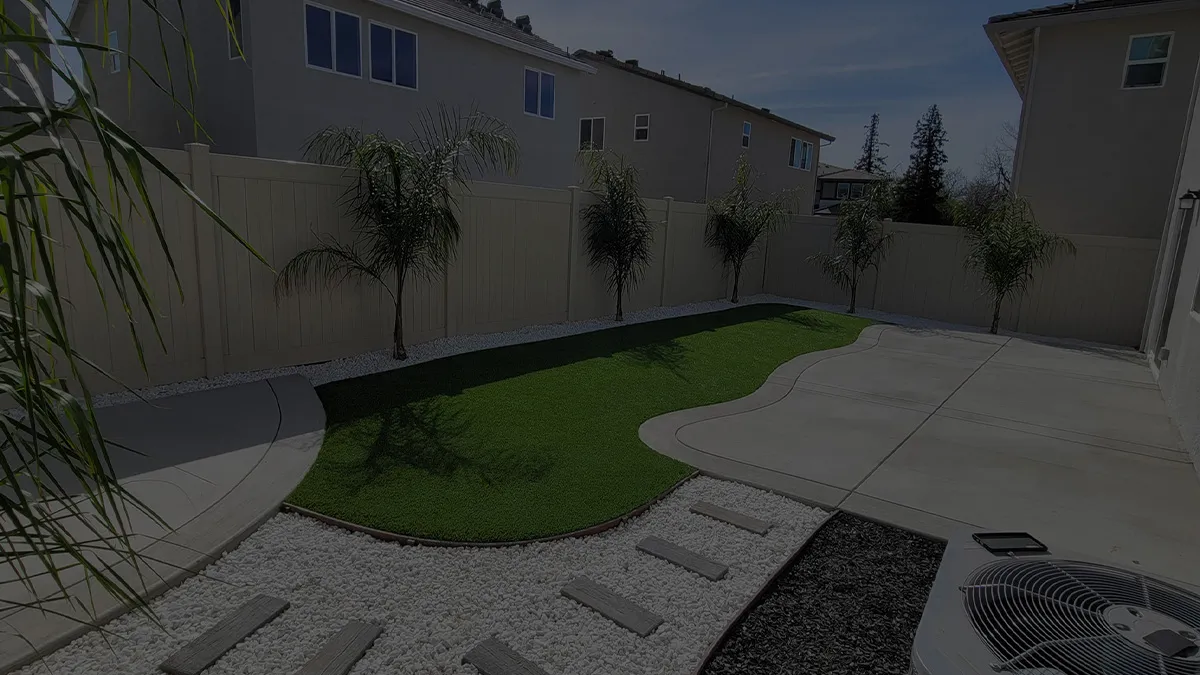 Completed backyard with curved artificial turf and new concrete patio at dusk