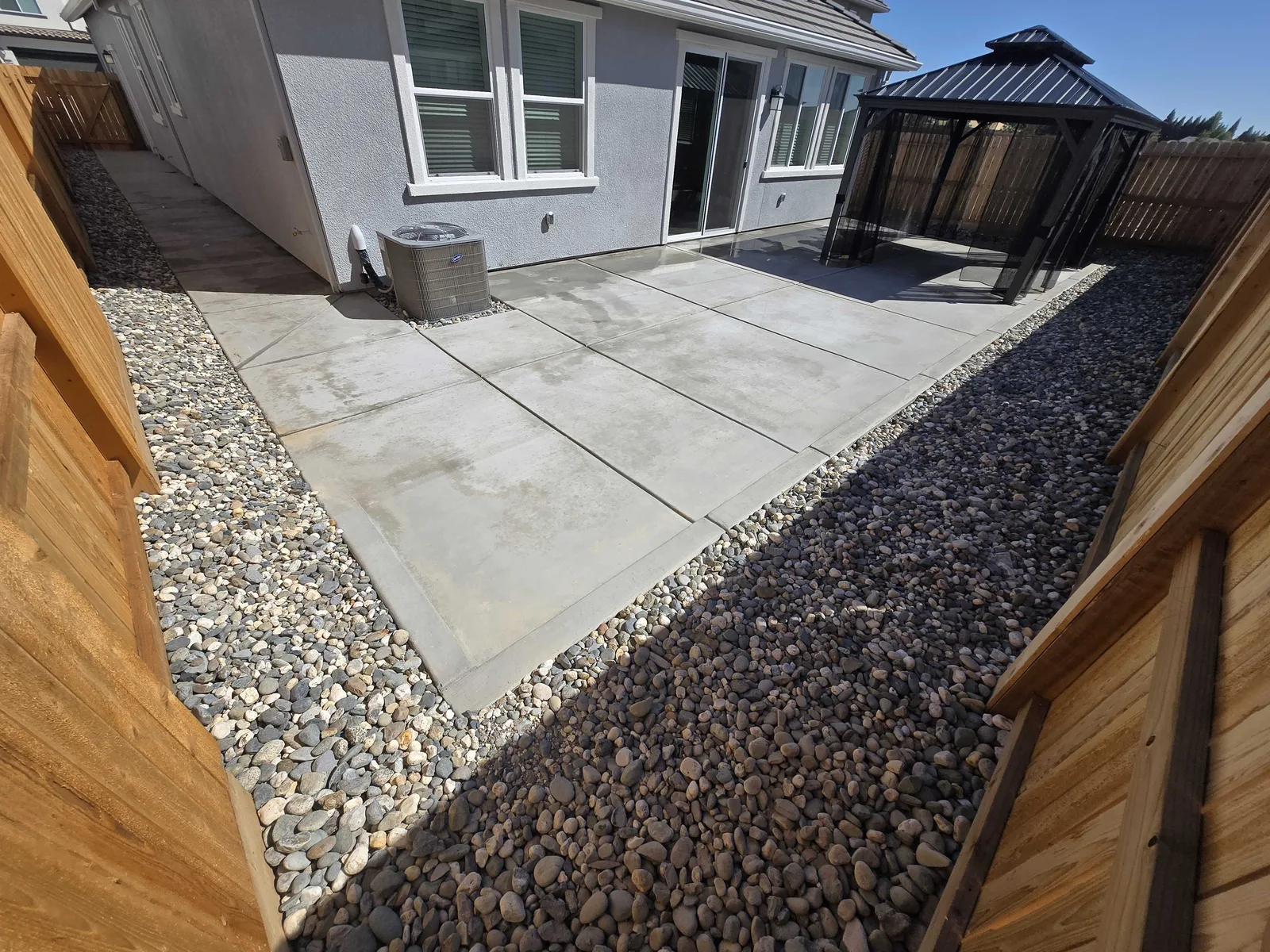 Backyard concrete patio edged with a gravel strip beside a gazebo