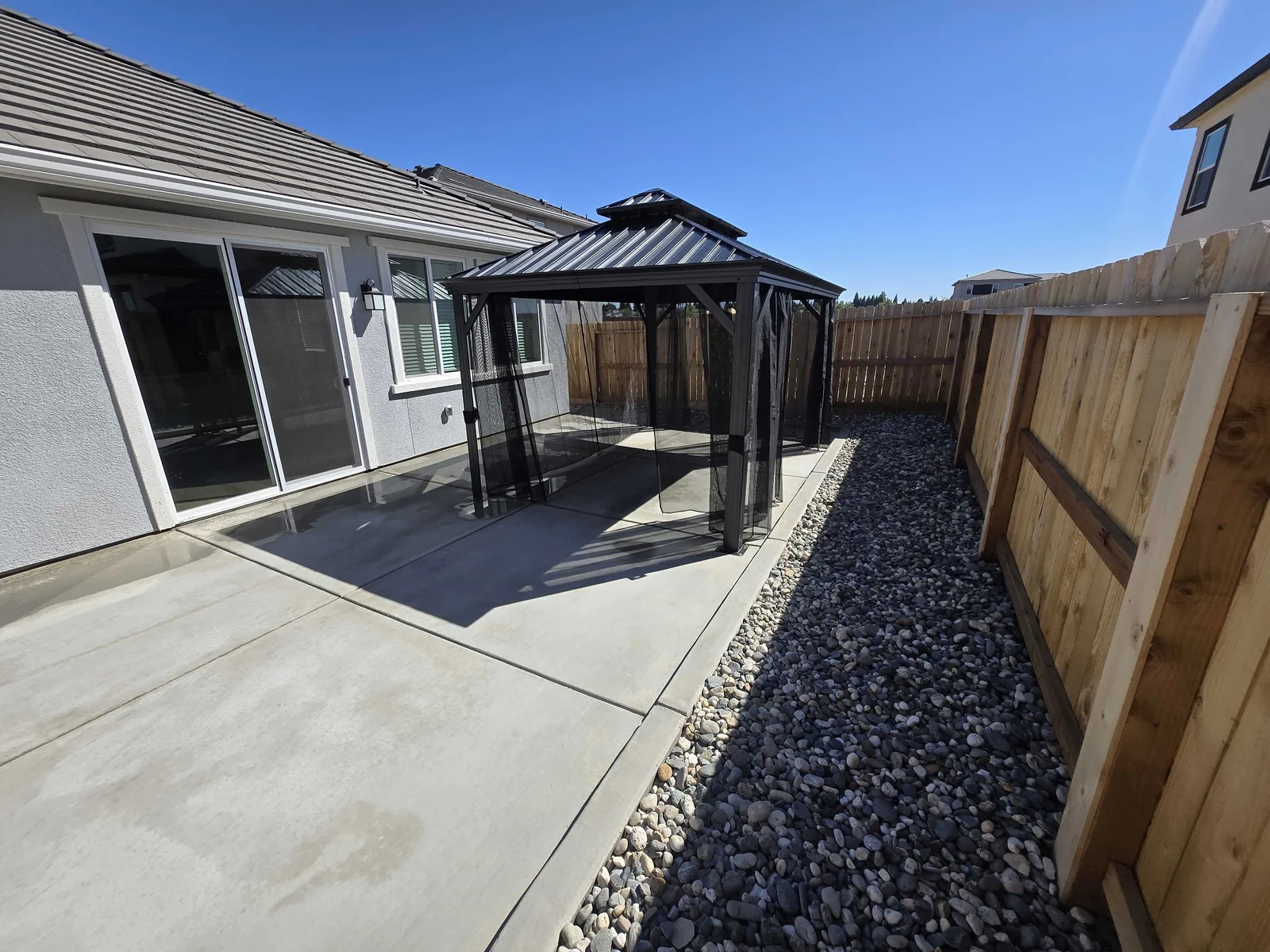 Concrete patio with a gazebo and a gravel border along the house