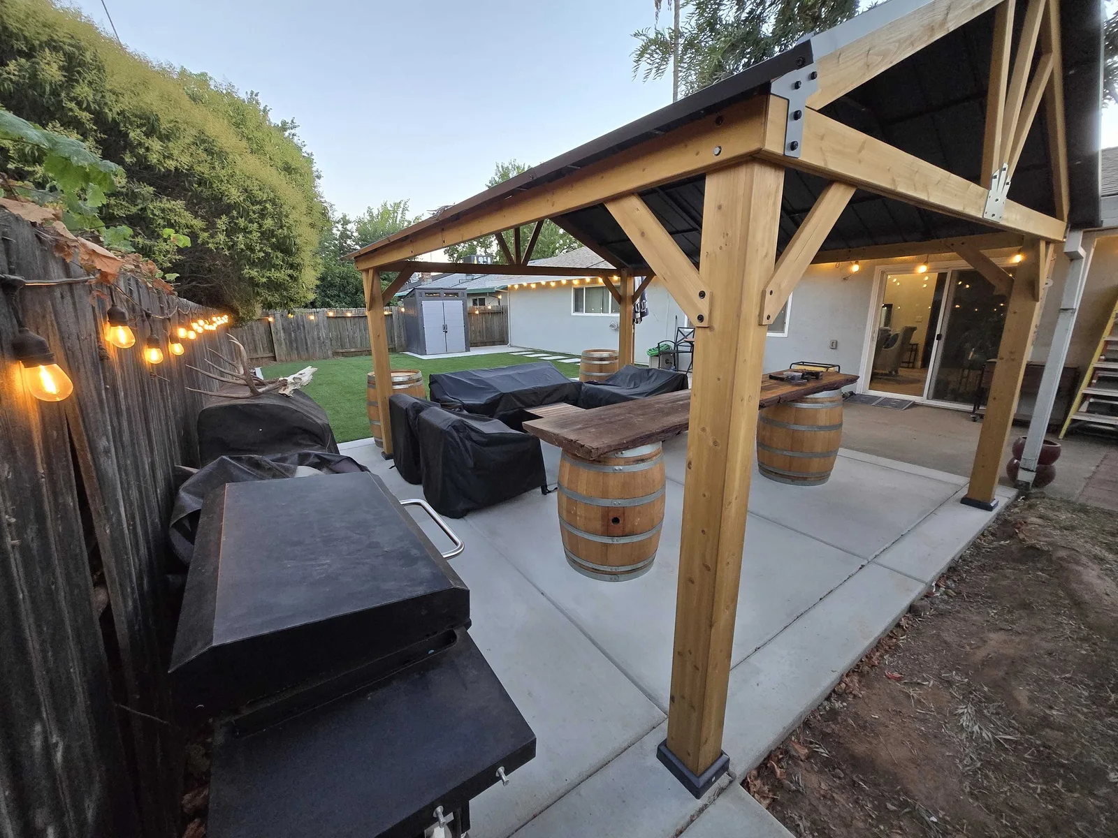 Concrete patio with a heavy-timber pavilion and string lights along the fence