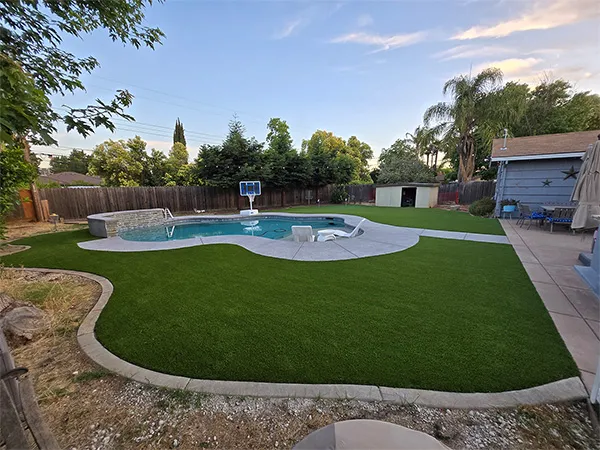 Backyard pool with white concrete deck, turf lawn and play area