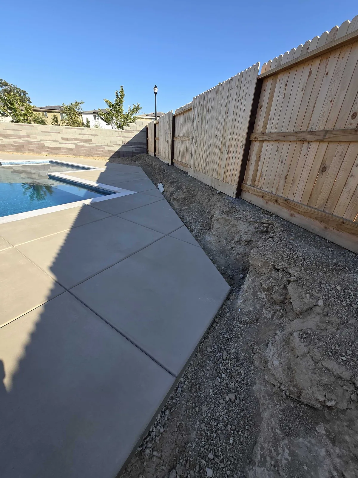 New concrete pool deck poured out to a wood fence line